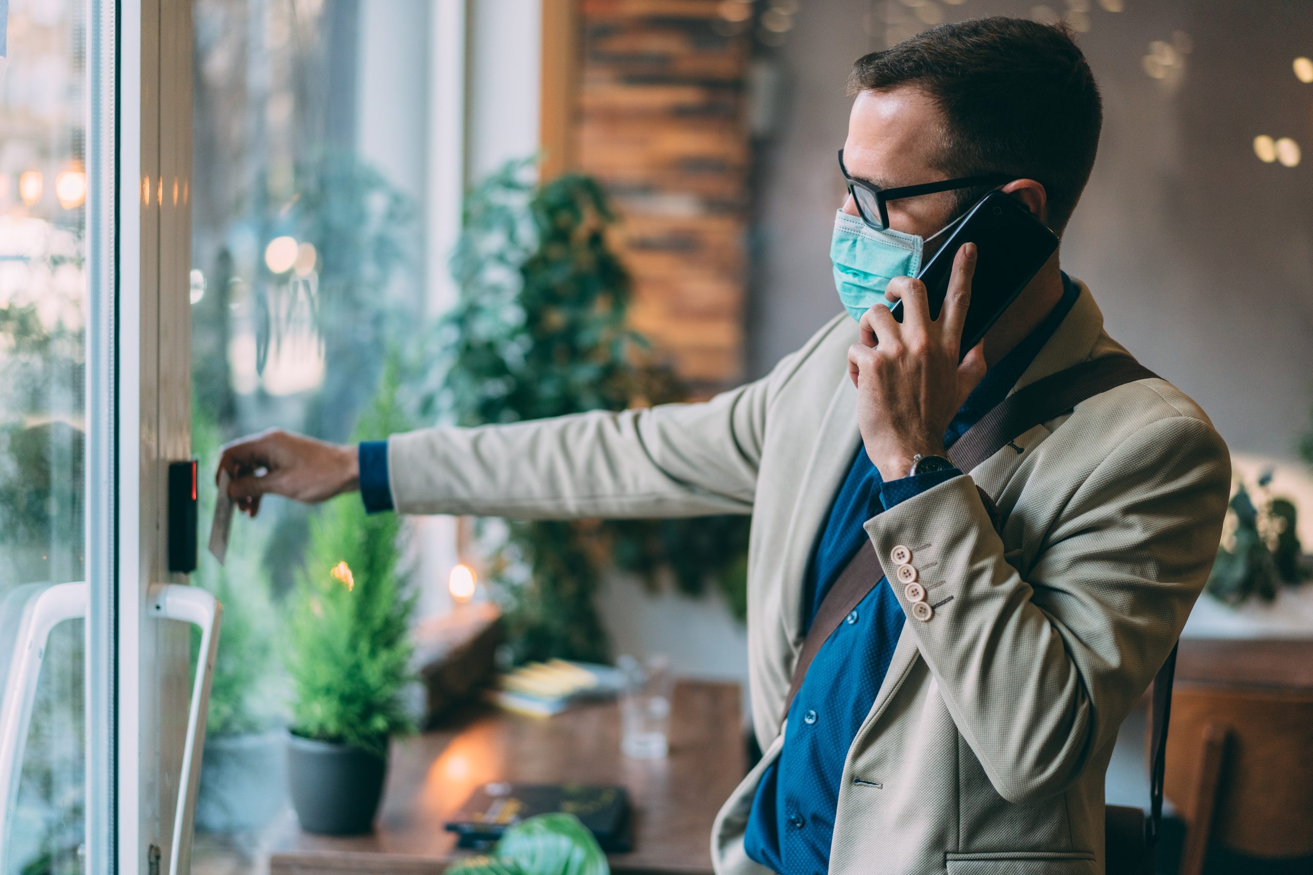 A man in a face mask uses a touchless entry system to securely enter the workplace